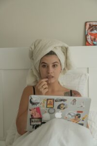 Vida Saudável Após os 40 Anos, moça com toalha na cabeça, pensando na cama com notbook na mão